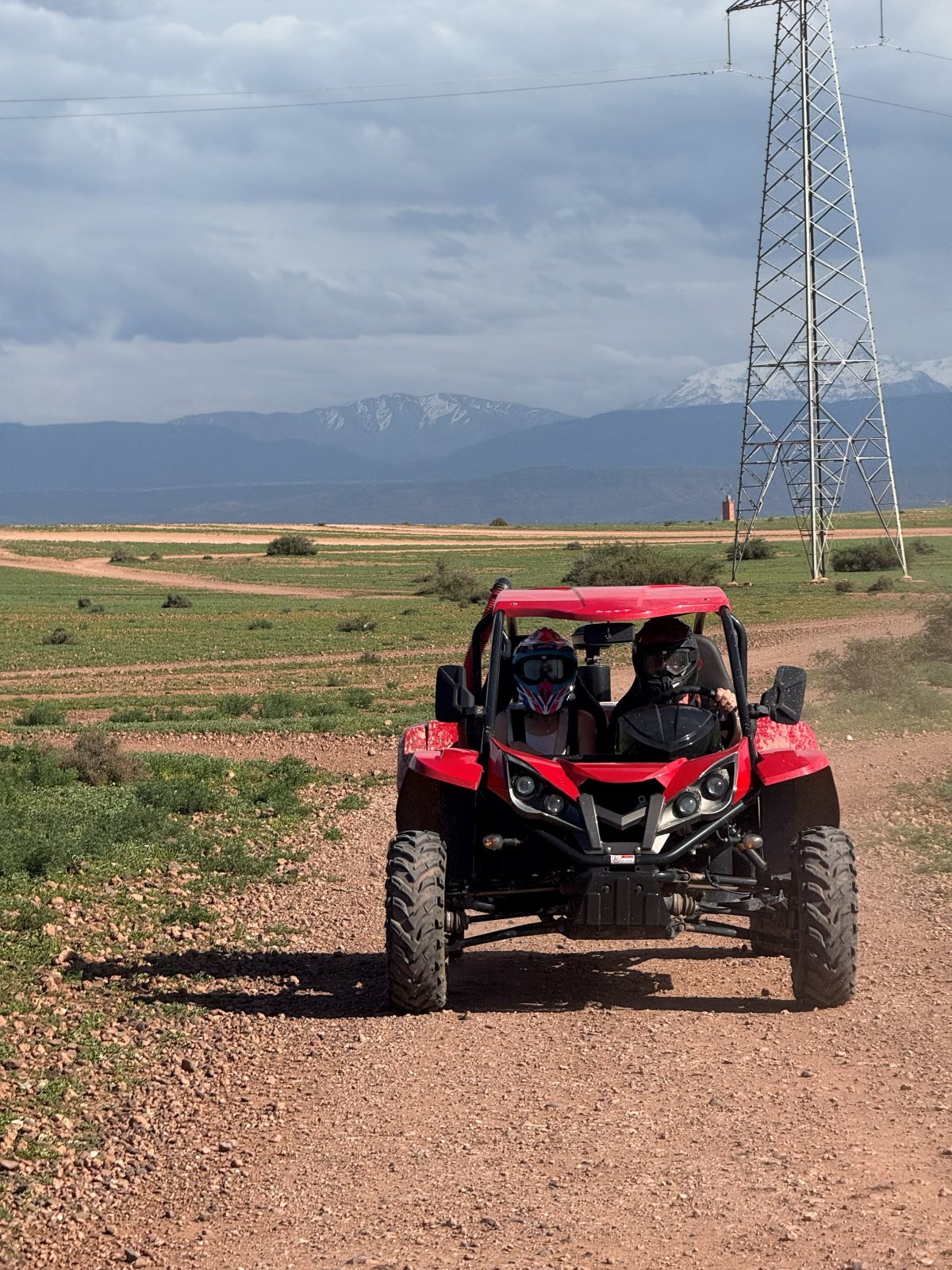 Buggy rojo con dos pilotos en una pista del desierto, con las montañas del Atlas al fondo, cerca de Marrakech